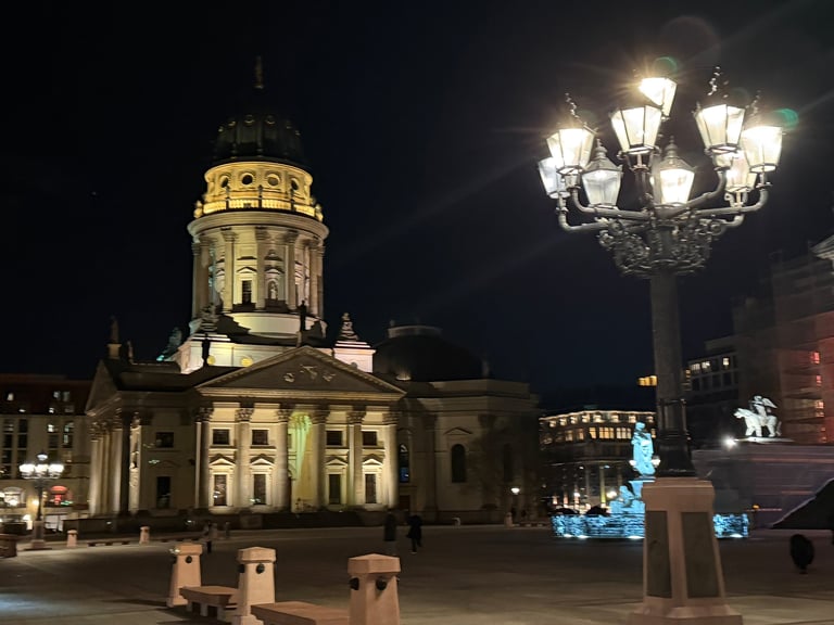 Illuminated historic domed cathedral at night in a European city square with street lamps and surrounding buildings